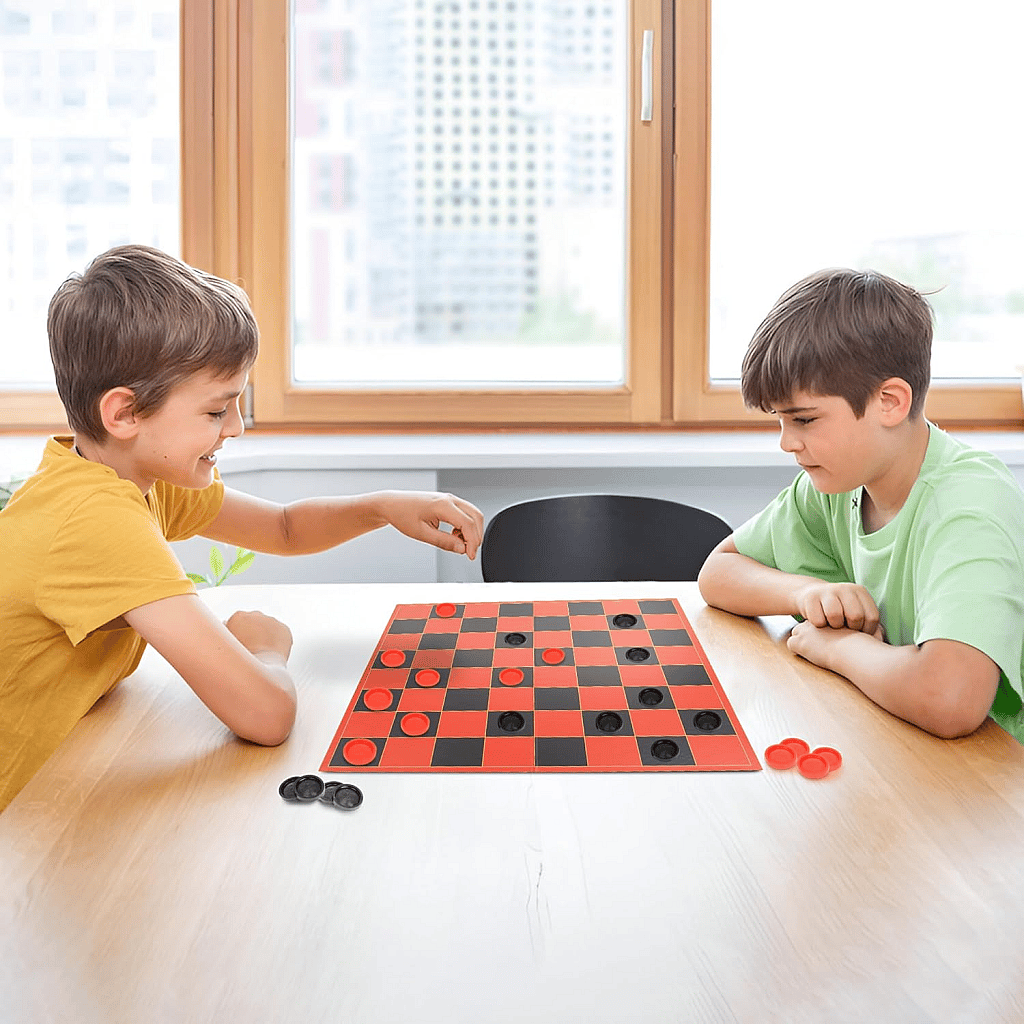 two young boys playing checkers board game on a table in a brightly lit room. The boys are smiling and concentrating on winning the game.