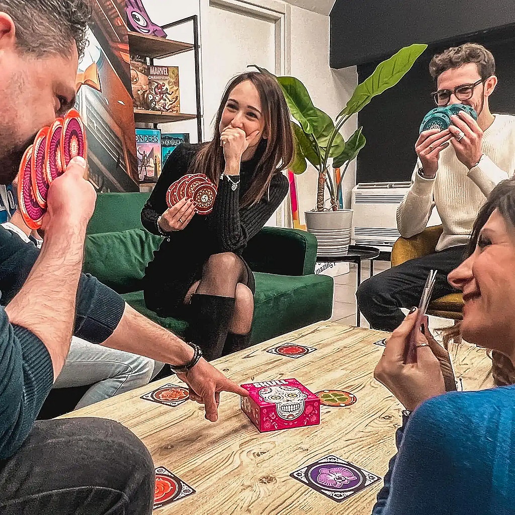 group of friends playing the bluffing tile board game Skull. In a living room, laughing, smiling, and having fun.
