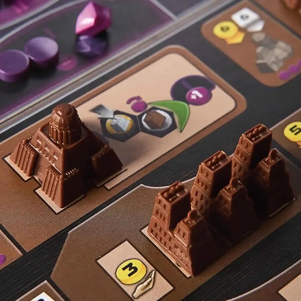 A close-up image of the Gaia Project game board, showcasing the detailed brown plastic building components, including a pyramid-like structure and a city cluster, next to various tokens and card art.