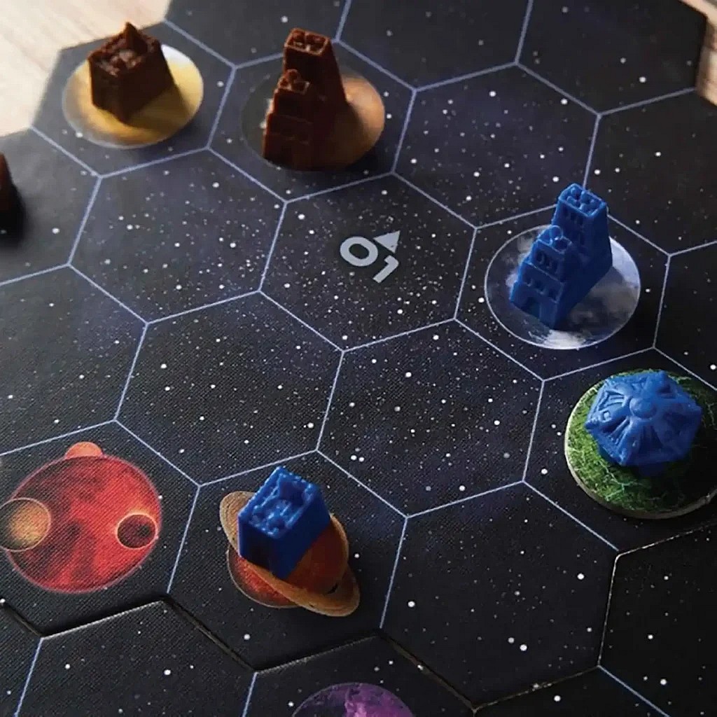 A close-up image of the Gaia Project game board showing several hexagonal star map tiles, with various brown and blue plastic building components placed on planet spaces, set against the dark, star-filled background.