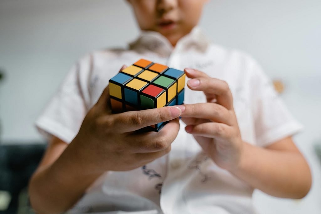 Focused child solving a Rubik's Cube indoors, highlighting intellect and problem-solving.