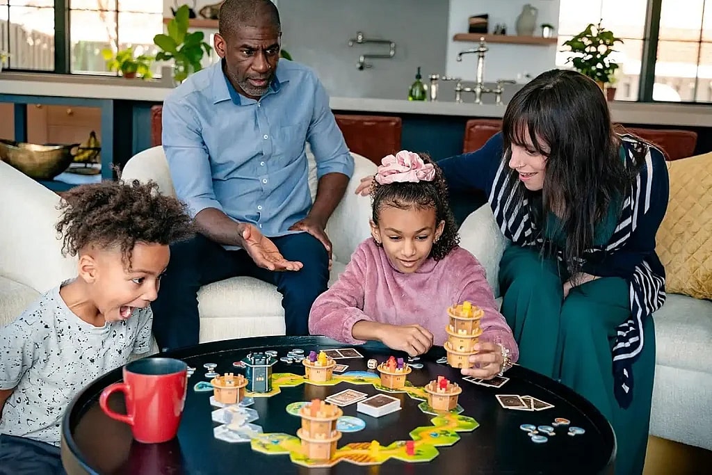 Family of four, 2 kids and 2 adults playing the wandering towers strategy board game, laughing, smiling, and having fun in a living room table on a couch