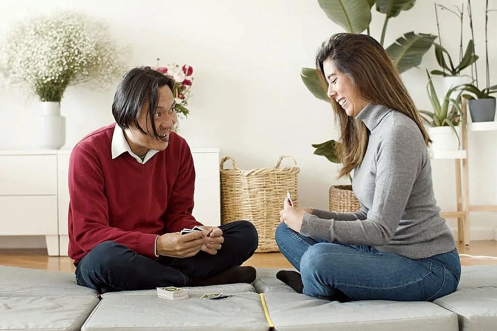 Happy couple enjoying a card game at home, sitting on floor cushions in a cozy setting.