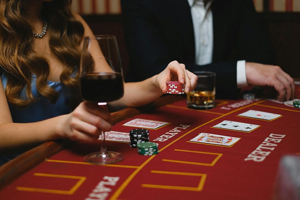 A blackjack game with drinks, featuring wine and chips on a casino table. A women is doubling down on her balckjack hand