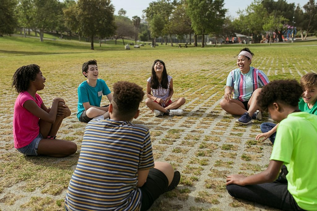 Diverse group of children laughing and playing games outdoors in a park setting.