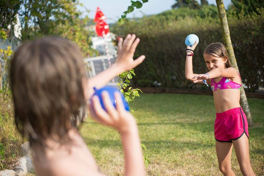 Two children engage in a fun water balloon fight during a sunny day outdoors.
