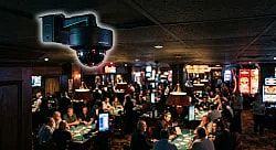 security camera outlined with a soft glow overlooking a casino floor with players and tables playing card games.