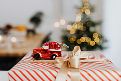 A red toy car with ornaments on a striped Christmas present in a cozy setting.