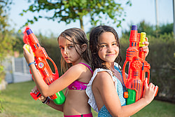 Two girls in vibrant swimsuits playing with water guns outdoors on a sunny day.