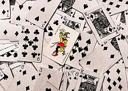 A vibrant joker card stands out in a scattered deck of monochrome playing cards.