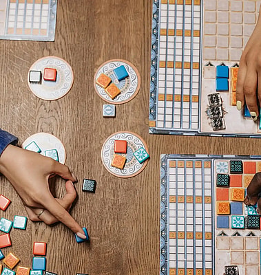 Hand pointing to a classic board game setup, with boards, cards, tokens, and chips