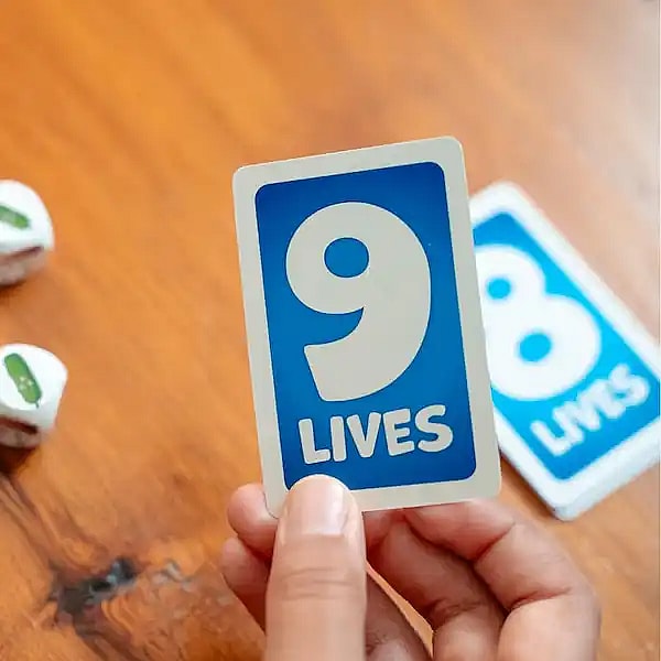hand holding a 9 lives card from the card and dice game Cats vs Cucumbers. with a wooden table in the background